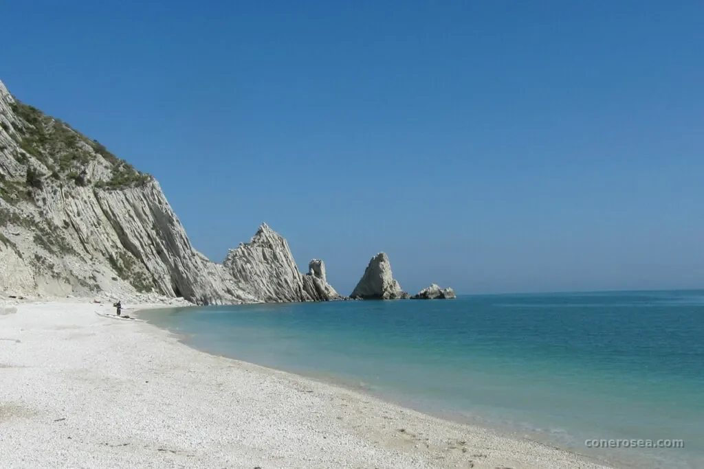 La spiaggia bianca delle Due Sorelle ai piedi della falesia, con i celebri faraglioni sullo sfondo