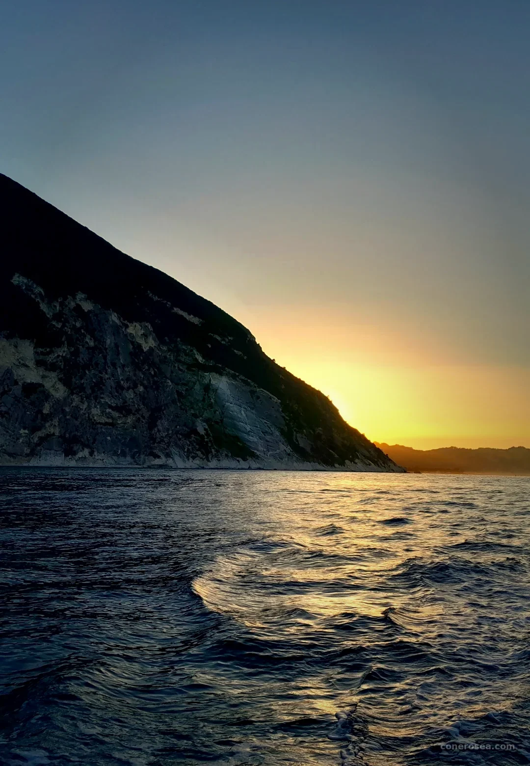 Il sole che tramonta dietro la scogliera del Monte Conero, con riflessi dorati sul mare Adriatico