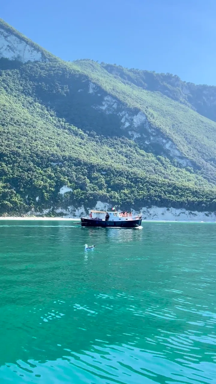 Il promontorio del Monte Conero che scende sul mare, con la barca sulle acque smeraldo