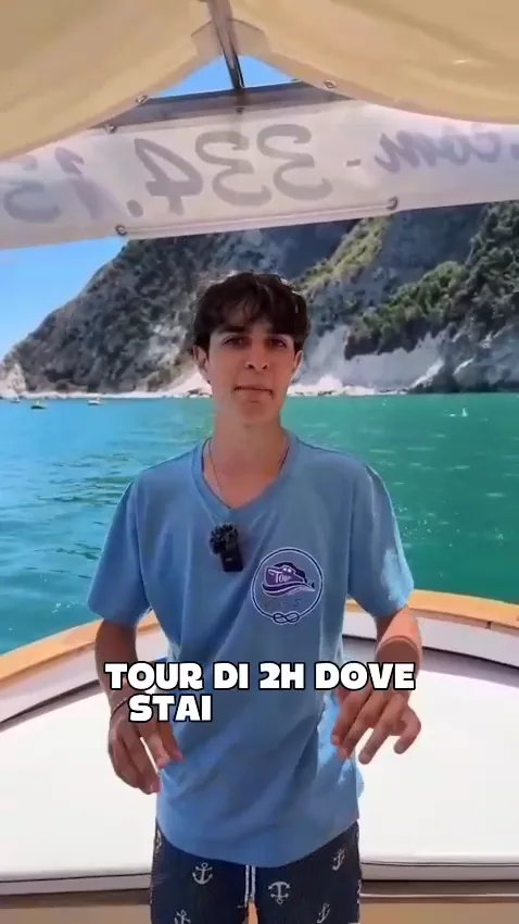 Lo skipper di Conero Sea a bordo della barca davanti alle falesie e alle acque verde smeraldo del Conero