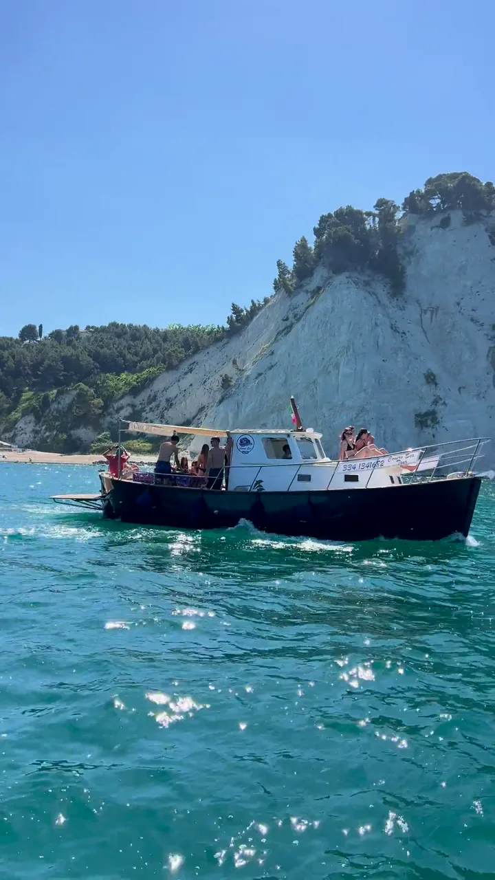 La barca in sosta sulle acque smeraldo ai piedi delle falesie bianche del Conero